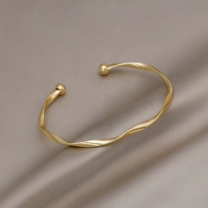 Dettaglio di un bracciale aperto intrecciato oro con sfere alle estremità su raso