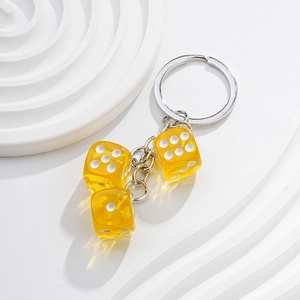 Macro shot of three transparent yellow resin dice on a metallic keychain against white waves