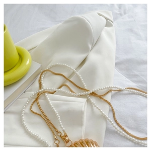 Detail of layered gold snake chain and pearl necklace with a polished seashell pendant