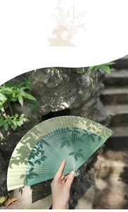 Detail of green gradient folding fan with hollow patterns against garden background