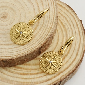 18K gold plated stainless steel hoop earrings with starburst coin charms on wood