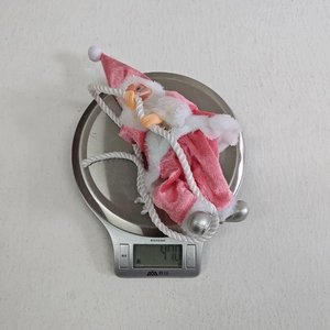 Pink Santa Claus resin ornament on white rope with bells shown on weight scale