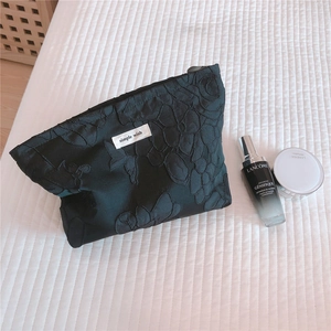Detail of black floral jacquard makeup bag with 3D embossed flowers and brand label