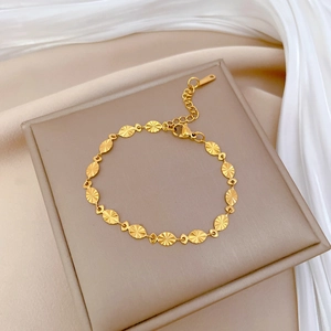 Close-up of gold oval sequin link chain bracelet with lobster clasp on beige cushion