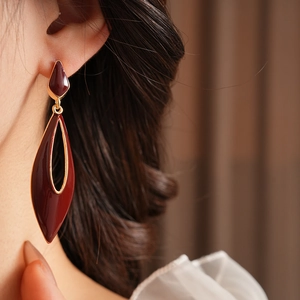 Close-up of vintage golden drop earrings with dark red enamel worn by a model