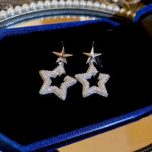 Close-up of star-shaped zircon earrings on blue velvet with decorative pearls