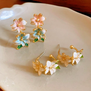 Detail of floral enamel earrings with pastel petals and gold plating on ceramic tray