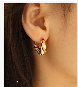 Macro detail of gold-plated twisted hoop earrings with black and white enamel stripes