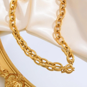 Detail of chunky gold chain necklace with classic OT clasp on white silk background