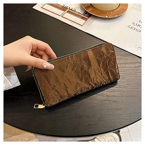 Brown velvet zipper wallet being held by a hand on a table with a lifestyle magazine