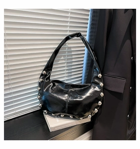 Detailed view of black patent leather crescent bag featuring silver punk stud accents