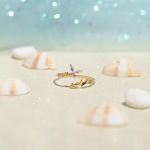 Macro detail of a golden butterfly ring with opal wings and zircons on white sand