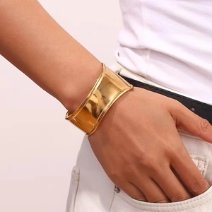 Detail of 18K gold-plated wide wave cuff bracelet with polished finish on female wrist