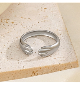 Gros plan d'une bague mains qui s'enlacent en argent sur socle en pierre beige poli