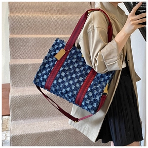Detail view of denim tote bag with frayed edges and red braided strap worn by a model