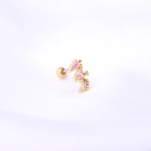 Détail macro du piercing hippocampe avec zircons roses et fermoir à boule dorée