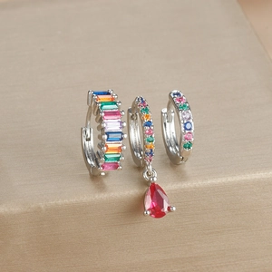 Macro detail of silver earrings set with colorful rainbow stones and red pear pendant