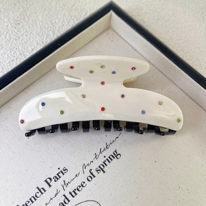 Detail of white acetate hair claw clip with colorful rhinestones and black inner teeth
