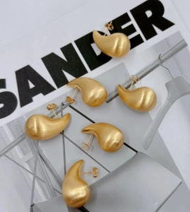 Detailed view of matte brushed gold teardrop stud earrings on minimalist fashion magazine