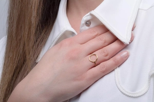 Detail of a gold minimalist hollow circular ring worn by a model in a white shirt