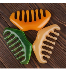 Three wide-tooth meridian massage combs in orange green and beige on a wood background