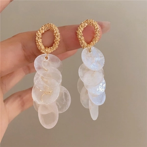 Golden round earrings with white shell tassel pendants on a clean grey background