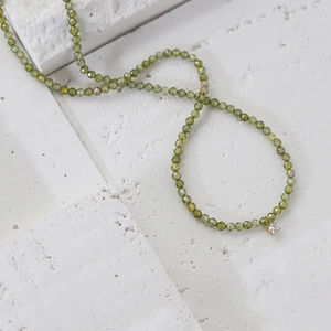 Detail of faceted olive green beaded necklace with sparkling clear zircon pendant