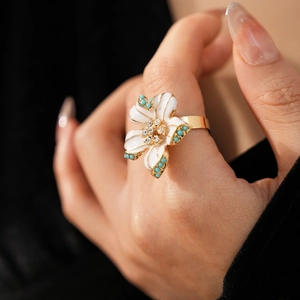 Gros plan d'une bague vintage dorée avec des pétales blancs et des perles turquoise