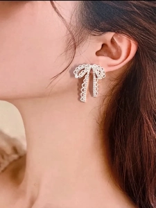 Close-up of a silver bow earring with shimmering zircons worn by a model in soft light