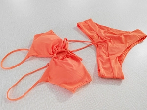Flat lay of coral orange bikini set featuring halter neck tie and pleated cutout details
