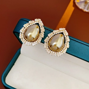 Detail shot of hollow teardrop pearl earrings with zircon inlay on a green jewelry box