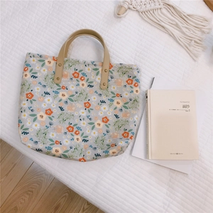 Detail of floral tote bag with orange print and rivet-reinforced handles on bed