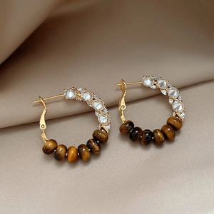 Macro shot of gold-plated hoop earrings with sparkling crystals and tiger eye beads