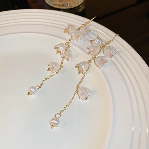 Détail de boucles d'oreilles muguet avec pétales blancs, chaînes dorées et perles