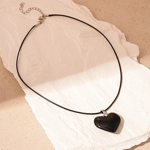 Detailed view of a dark vintage heart pendant with glossy finish on a black cord strap