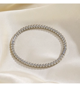 Macro shot of silver beaded bracelet with polished cylindrical clasp on silk background