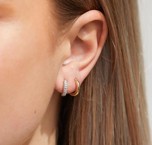 Macro shot of gold huggie hoop and silver pavé zircon earring stacked on a female ear