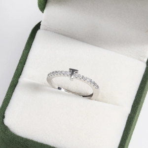 Detailed view of silver T-shaped letter ring with small diamonds in green jewelry box