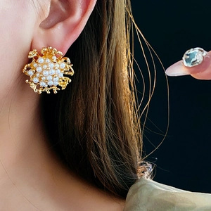 Dettaglio di orecchini vintage a fiore con perle bianche su base in metallo dorato
