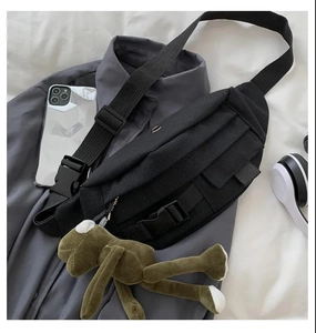 Detail of black canvas tactical chest bag on shirt with accessories and frog charm