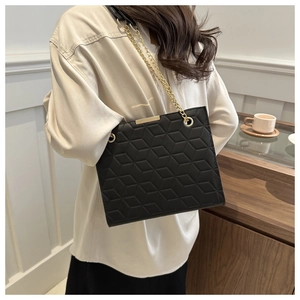 Detail of black leather tote bag with geometric quilted pattern and gold chain strap