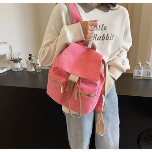 Mochila de lona rosa con cordón y cremalleras metálicas mostrada en un ambiente de cafetería