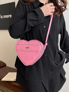 Pink heart-shaped crossbody bag made of faux leather with adjustable strap shown on model