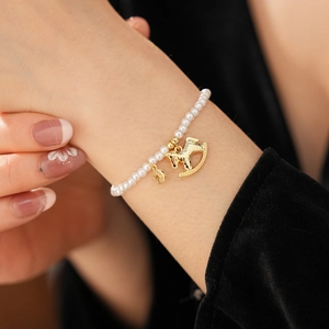 Close-up of pearl bracelet with gold horse charm and round pendant on woman's wrist