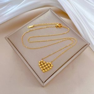 Gold stainless steel necklace with beaded heart pendant on beige box over white silk