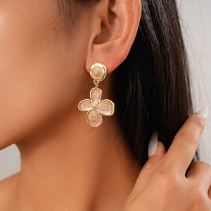 Close-up of gold flower earrings with pink enamel inlay worn by a model in a profile view