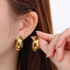 Polished golden teardrop stud earrings in stainless steel on a female model