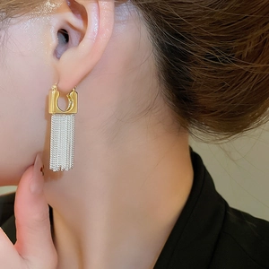 Close-up of 14k gold plated U-shaped earrings with long silver tassel chains on model