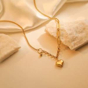 Detailed view of golden heart pendant on mixed chain over luxurious silk and white stone