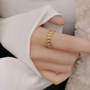 Detail of gold hollow woven ring featuring multi-row dots on a hand with a soft background